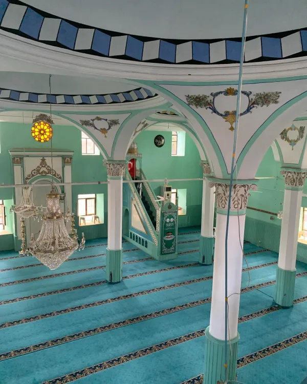 Açık yeşil duvarlar ve mavi desenli tavan ile iç mekânı gösteren geniş bir cami.