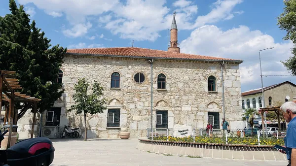 Tarihi Devlethan Camii, tuğla çatısı ve ince minaresi ile görünüyor. Önünde yürüyüş yapan insanlar var.