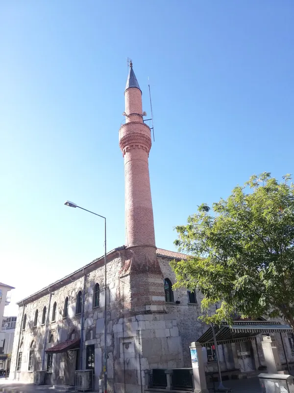 Açık mavi gökyüzü altında yükselen Devlethan Camii minaresi ve tarihi taş yapısı.