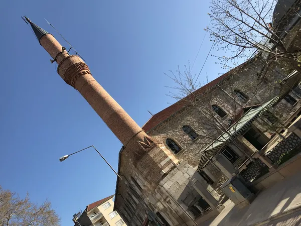 Yüksek minaresi ve taş işçiliği ile dikkat çeken Devlethan Camii, mavi gökyüzü altında görünüyor.