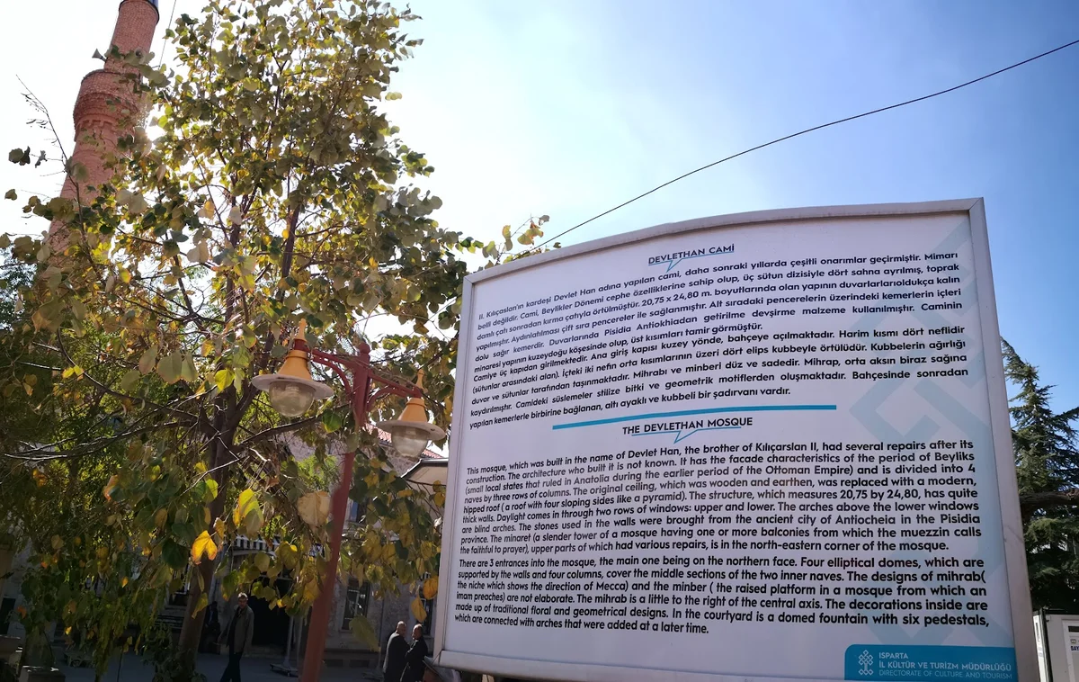 Tarih ve Mimari Güzellik - Bilgilendirme Panosu ve Doğal Çevresiyle Devlethan Camii! Devlethan Camii'nin bilgilendirme panosu, arka planda minare ve sonbahar ağaçlarıyla çevrili.