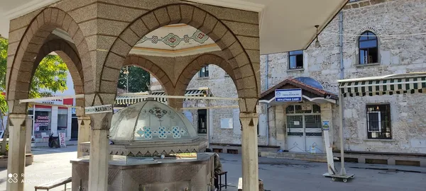 Geleneksel bir çeşme, süslü kubbe ve tarihi cami görünümüyle huzurlu bir mekan.