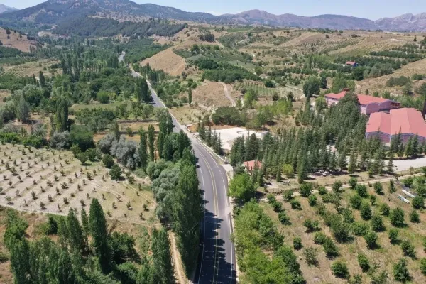 Yeşil ağaçlarla çevrili, dağlık ve ormanlık bir alanda yollar ve tarım alanları görünmekte.