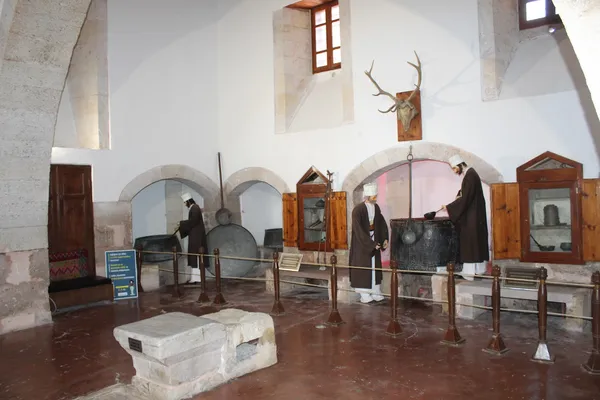 Tarihi türbe iç mekanında büyük bir kazan ve geleneksel kıyafetler giymiş figürler yer alıyor.