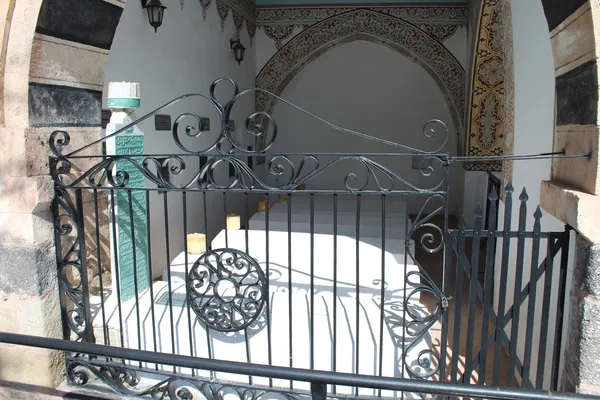 Beyaz örtülü mezarların demir parmaklıkla çevrelendiği aydınlık iç mekan.