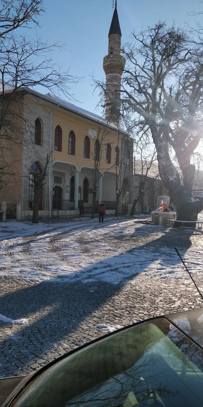 Karlı sokakta eski cami minaresi ve yürüyüş yapan insanlar gözüküyor.