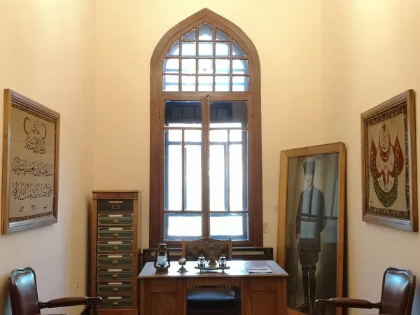 Tarihi bir odanın iç mekanında Osmanlıca yazılı tablolar ve ahşap masa yer alıyor.