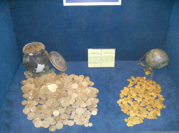 Mavi arka planda sergilenen bronz ve altın paralar vitrinde yer almakta.