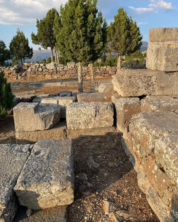 Antik yapı kalıntıları, yeşil ağaçlar ve hafif bulutlu gökyüzü ile doğal bir manzara sunuyor.