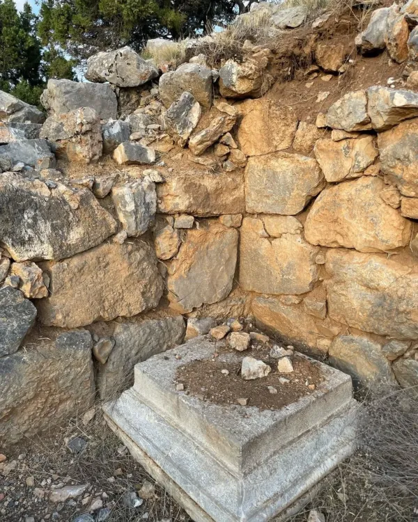 Doğal taşlardan yapılmış tarihi bir duvar köşesi ve yeşil ağaçlar.