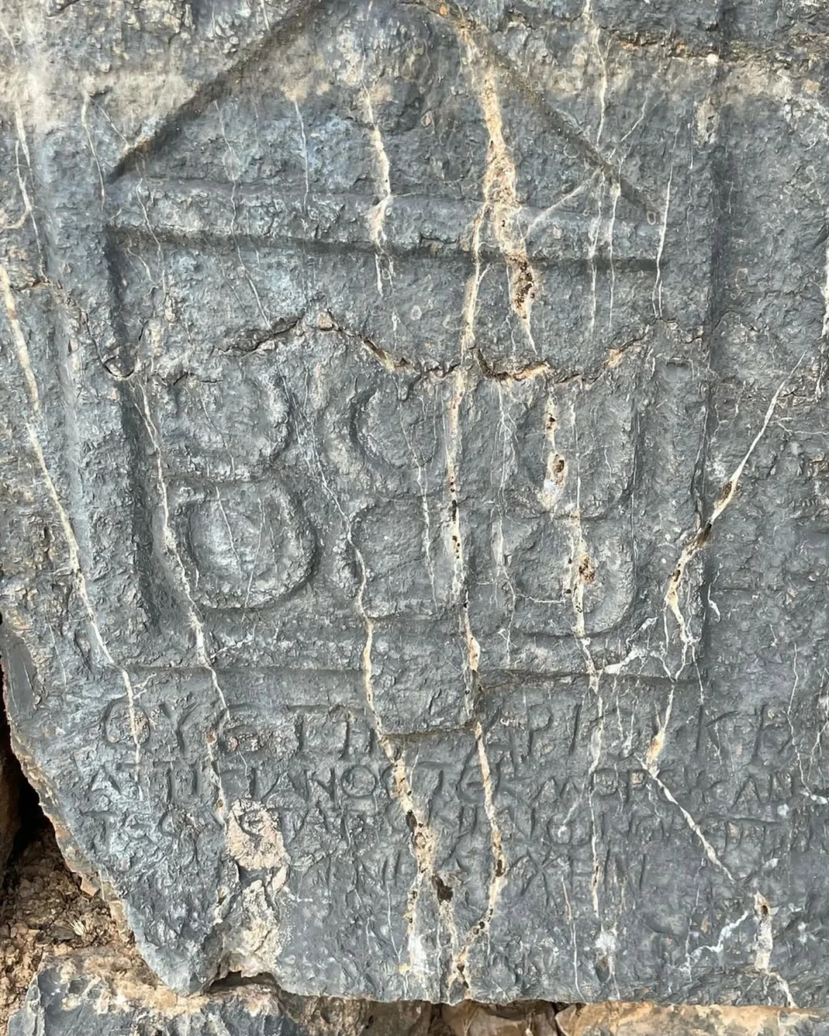 Koyu gri taş üzerinde yazılar ve semboller, doğal dokusu ile dikkat çekiyor.