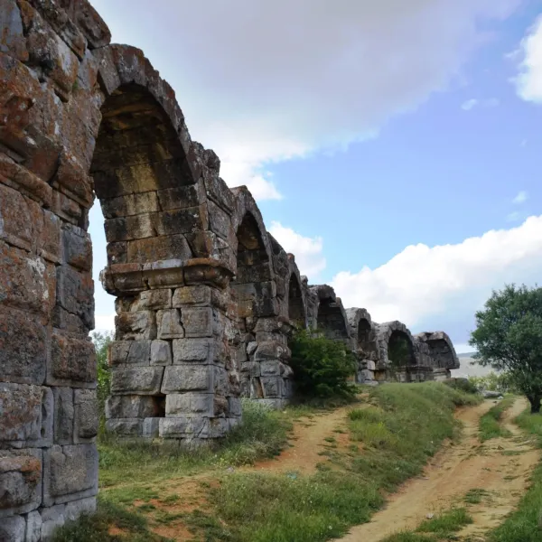 Yüksek kemerli antik su kemerleri, bitki örtüsüyle kaplı ve mavi gökyüzüyle çevrili.