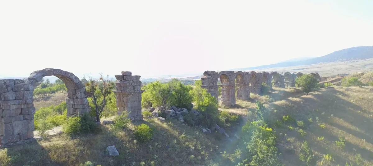 Yeşil bitki örtüsüyle kaplı arazide antik su kemerleri ve arka planda dağlar