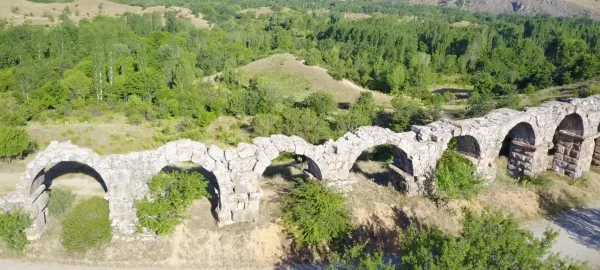 Eski taş su kemeri, yeşil ağaçlarla çevrili, bazı kemerleri yıkılmış.
