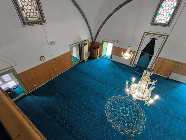 Geniş cami iç mekânı, yuvarlak tavan, mavi halı ve büyük avize ile aydınlık bir atmosfer sunuyor.