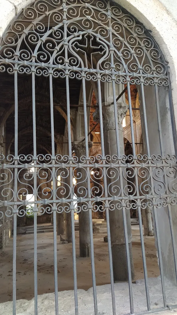 Demir parmaklıklarla kapatılmış tarihi yapının iç kısmı, yüksek sütunlar ve taş destekler ile dikkat çekiyor.