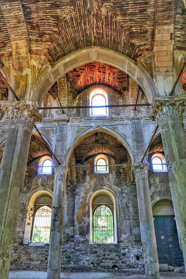 Eski bir yapının yüksek kemerli tavanı, taş sütunları ve ahşap kirişleri görünmekte.