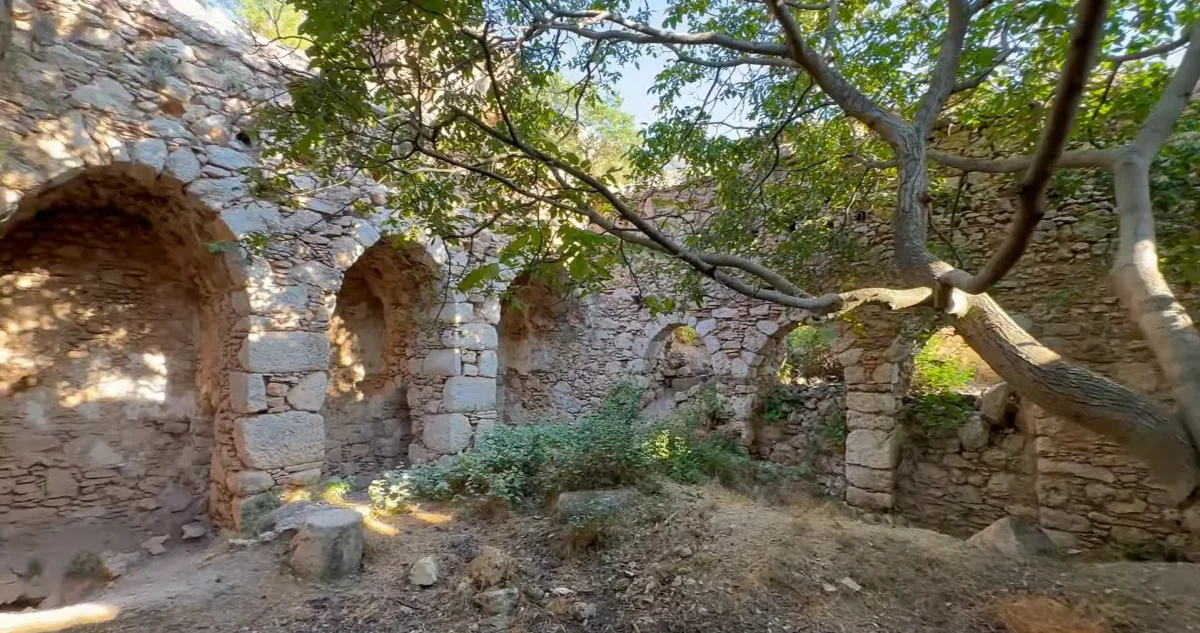 Tarihi Aya Georgios Kilisesi'nin kalıntıları, yeşil bitkilerle çevrili doğal ortamda görüntüleniyor.