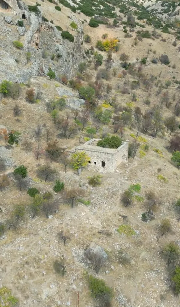 Yamaçta terkedilmiş taş yapı, çevresindeki doğal alan ve ağaçlarla birlikte görünmekte.