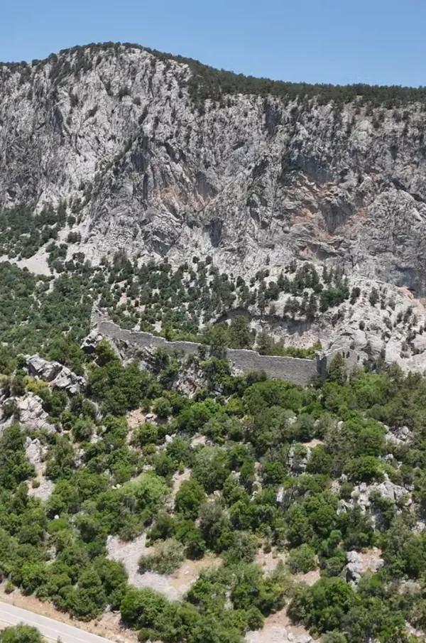 Yüksek dağların eteğinde, yeşil alanda yıkık taş sur görünümü.