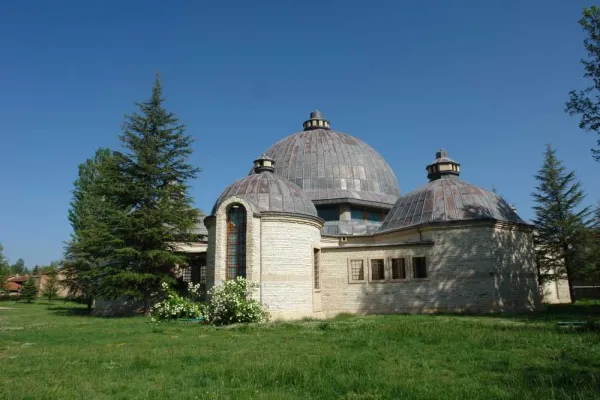 Geniş yeşil alanda ilginç mimari yapının kubbeleri ve taş duvarları görünüyor.