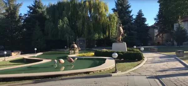 Bahçede su, pembe flamingo heykelleri, büyük ağaçlar ve taş döşeme dikkat çekiyor.