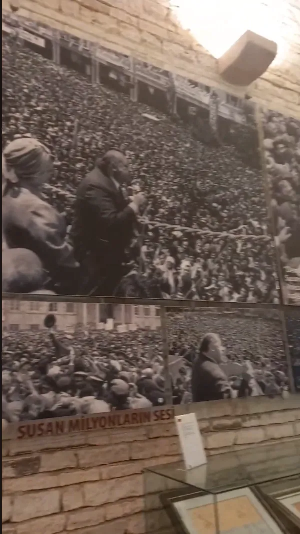 Siyah-beyaz fotoğraflarla dolu sergi alanında kalabalık bir topluluk ve konuşmacı