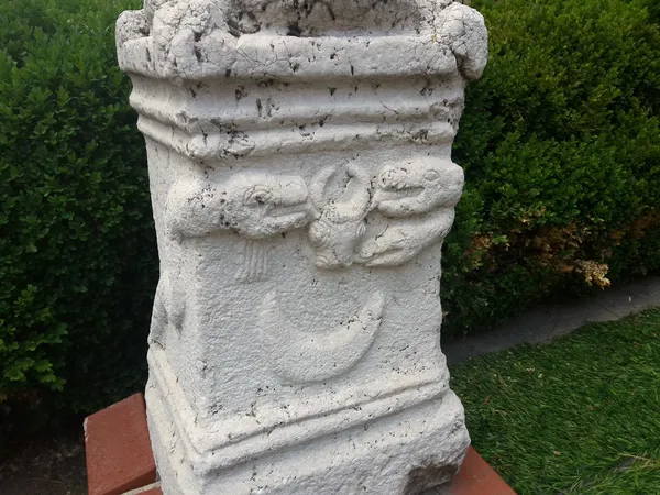 Taş sütun, kabartmalar ve hayvan figürleriyle çevrili yeşil bitki örtüsü