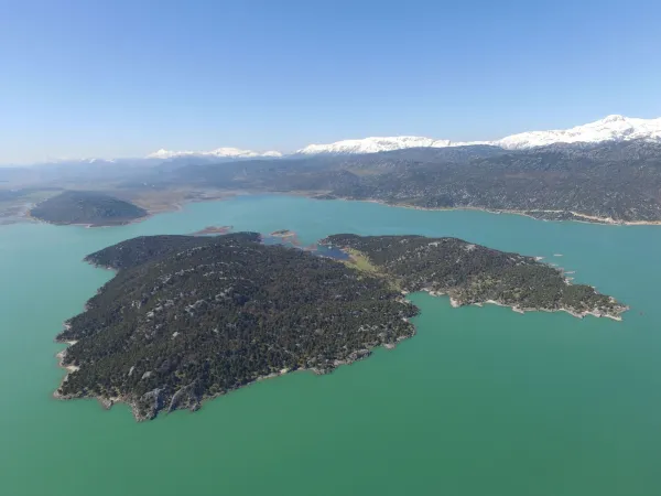 Yeşil adacıklar ve karla kaplı dağlarla çevrili huzurlu Beyşehir Gölü manzarası.