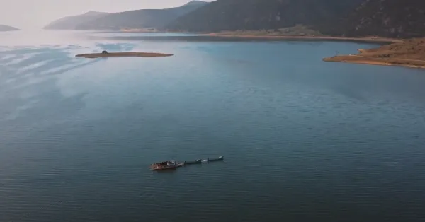 Sakin su yüzeyinde yüzen tekne ve çevresindeki doğal manzara