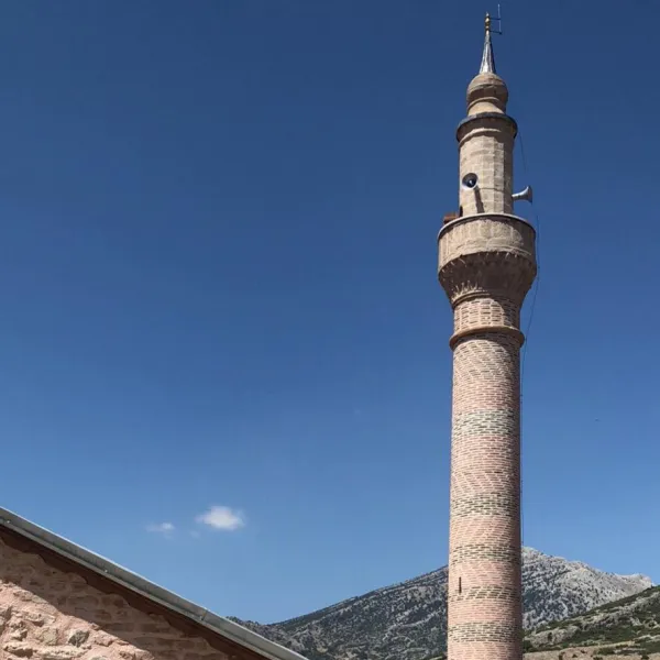Mavi gökyüzü altında tuğla desenli cami minaresi ve dağlık manzara