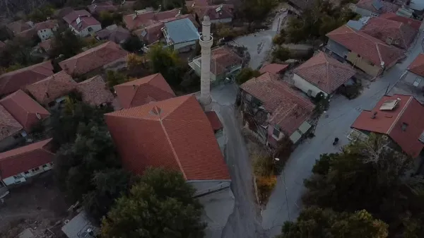 Kırmızı kiremit çatılı evler ve yüksek bir minare ile huzurlu bir köy manzarası.