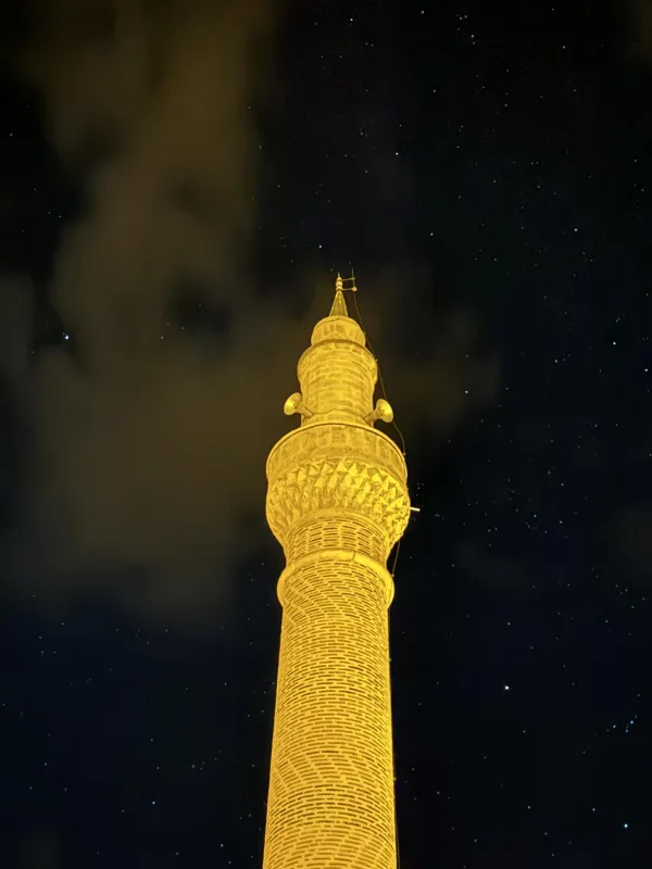 Gece ışıkla aydınlatılmış yüksek minare, yıldızlı gökyüzü ile çevrili.