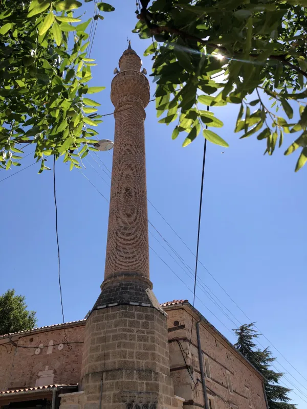 Minare ve tarihi bina, mavi gökyüzüyle aydınlık bir gün.