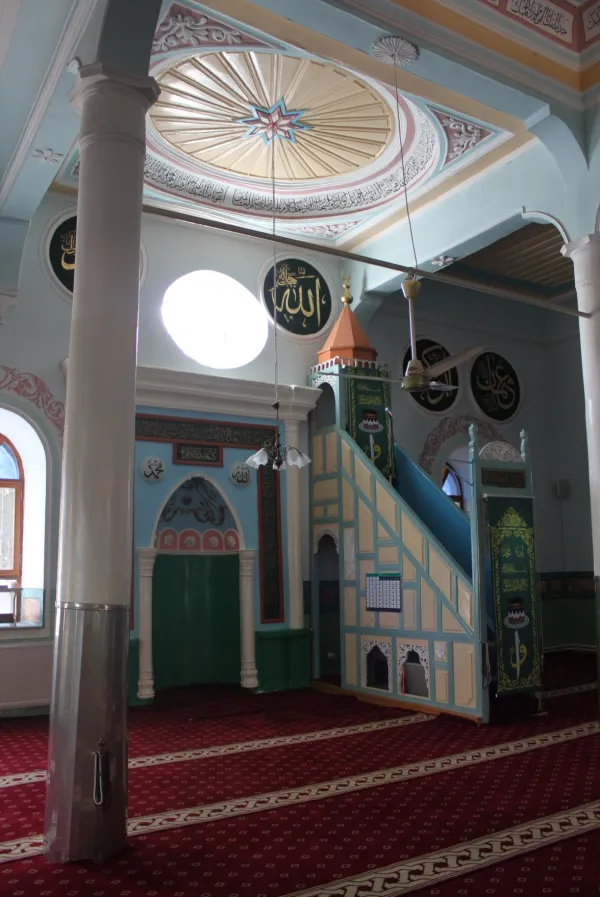 Pastel tonlarda duvarları, süslü tavanı ve yeşil minberi ile huzur verici cami iç mekanı.
