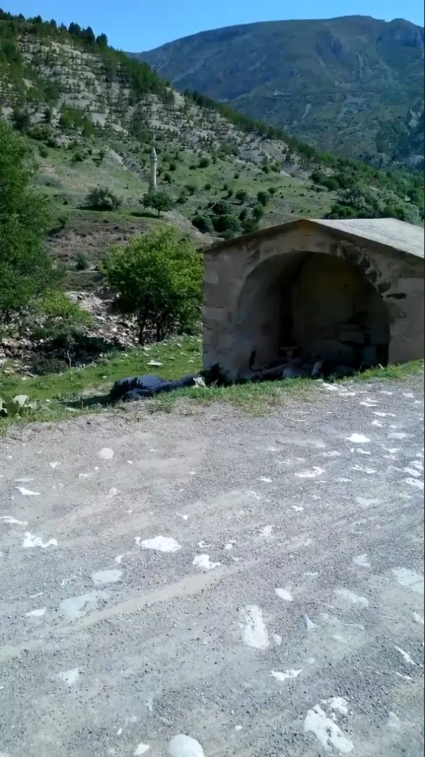 Eski taş yapı, yeşil ağaçlar ve dağ manzarası ile doğal ortam.