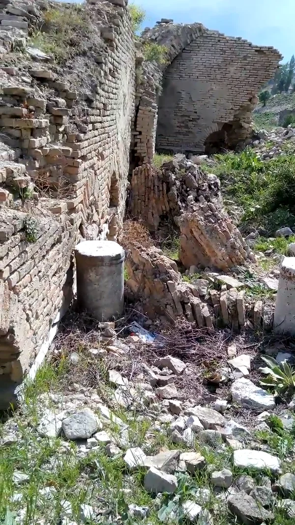 Yıkılmış tuğla duvarlar arasında yeşil bitki örtüsü ve silindirik beton yapılar