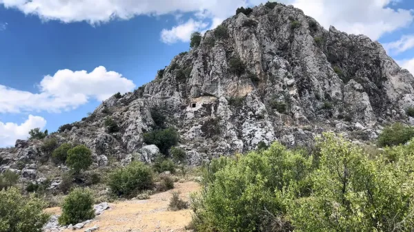 Sarp dağ ve ejderha şeklindeki kayalık alan, yeşil bitki örtüsüyle çevrili.