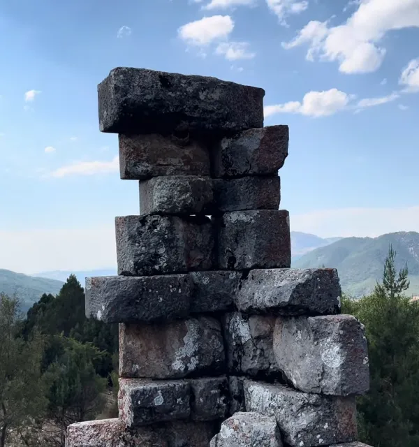 Taşlardan oluşan tarihi yapı, yemyeşil dağlar ve bulutlu gökyüzü ile çevrili.