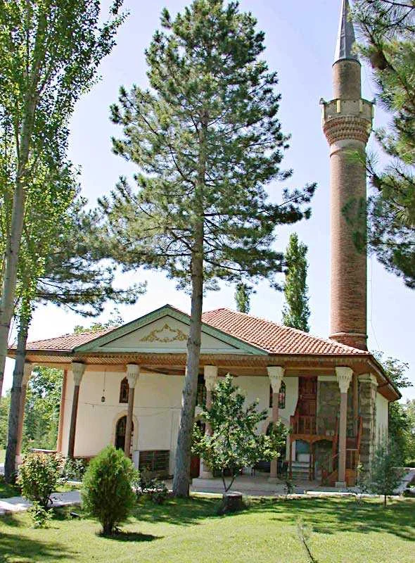 Yeşil ağaçlarla çevrili, beyaz duvarlı ve kırmızı çatılı Feyzullah Paşa Camii manzarası
