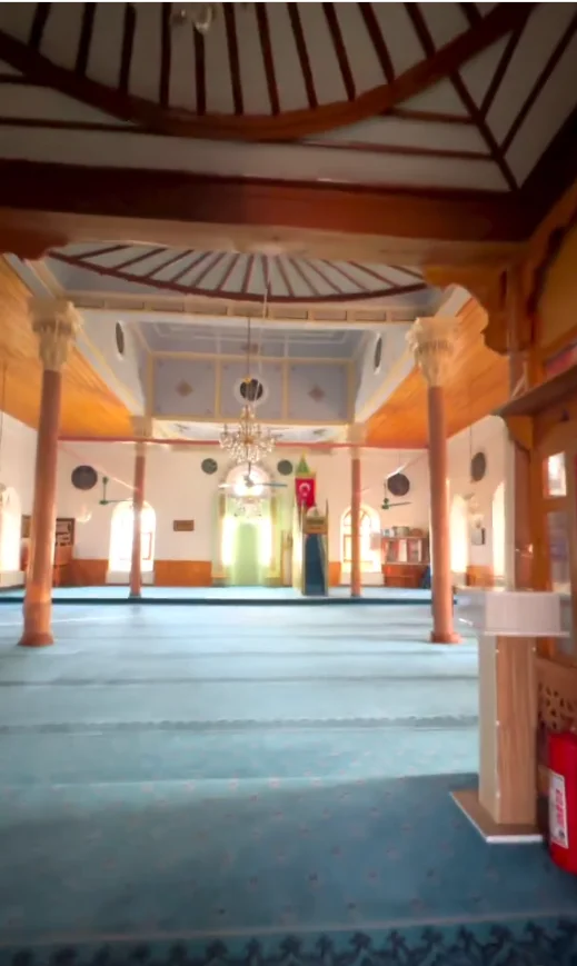 Geniş cami içi, mavi halı, ahşap tavan ve süslü duvarlarla donatılmış.