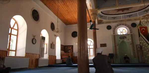Feyzullah Paşa Camii iç mekanında ahşap tavan, mavi halı ve dua eden insanlar