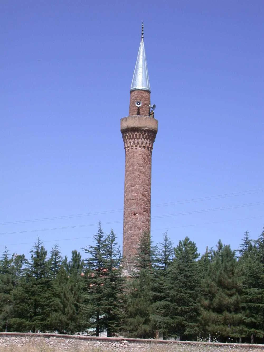 Küçükgökçeli Kırık Minare Camii, koyu renkli minaresi ve çam ormanıyla çevrili doğal bir manzara.