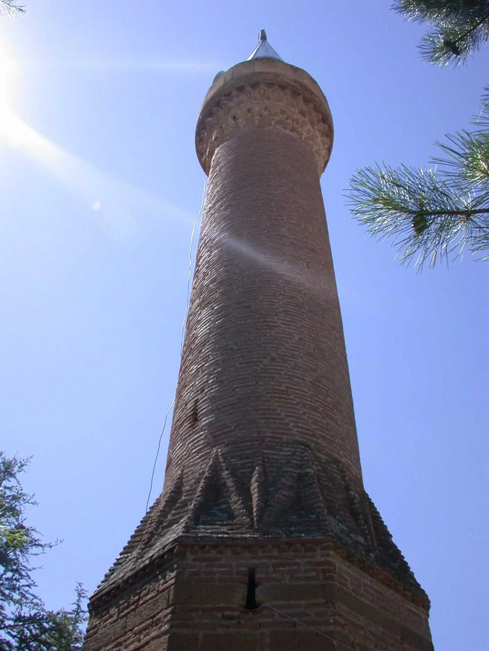 Ince ve yüksek kırmızı tuğla minare, güneş ışığı altında etkileyici siluetiyle yükseliyor.