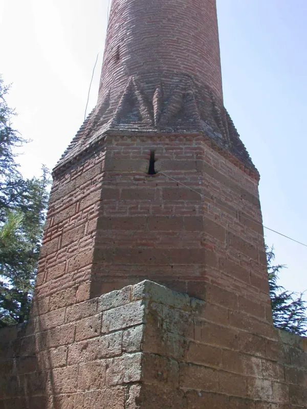 Eski taş yapının tuğla ile kaplı üst kısmı, yeşil ağaçlar ve mavi gökyüzü ile çevrili.