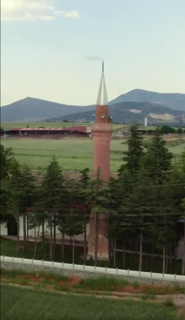 Yeşil alanda yükselen kırmızı tuğlalı uzun minare ve çevresindeki ağaçlar.