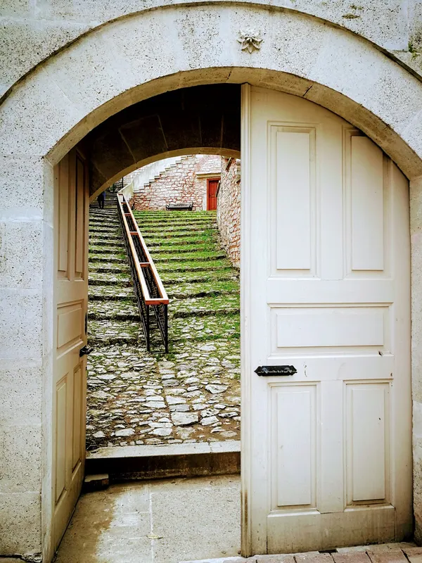 Açık kapıdan görülen taş zemin ve yeşil merdivenler, huzurlu bir atmosfer sunuyor.