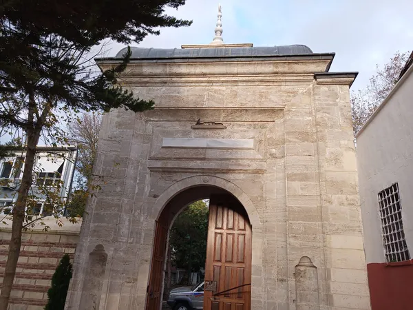 Tarihi bir yapının büyük taş arka kapısı, yeşil ağaçlar ve kubbe ile çevrili.