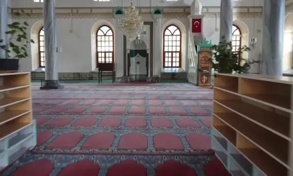 Alaaddin Camii iç mekanında kırmızı halı, avize ve ahşap raflar görünmektedir.
