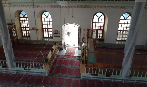 Geniş bir cami iç alanı, yüksek tavan ve ahşap çerçeveli pencerelerle huzur dolu bir atmosfer sunuyor.